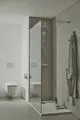 Moderne Duschkabine mit transparenten Wänden, Brausethermostat und Handbrause. An einer Wand hängt ein Handtuch. Ideal Standard Duschsystem sichtbar. Toilette im Hintergrund.